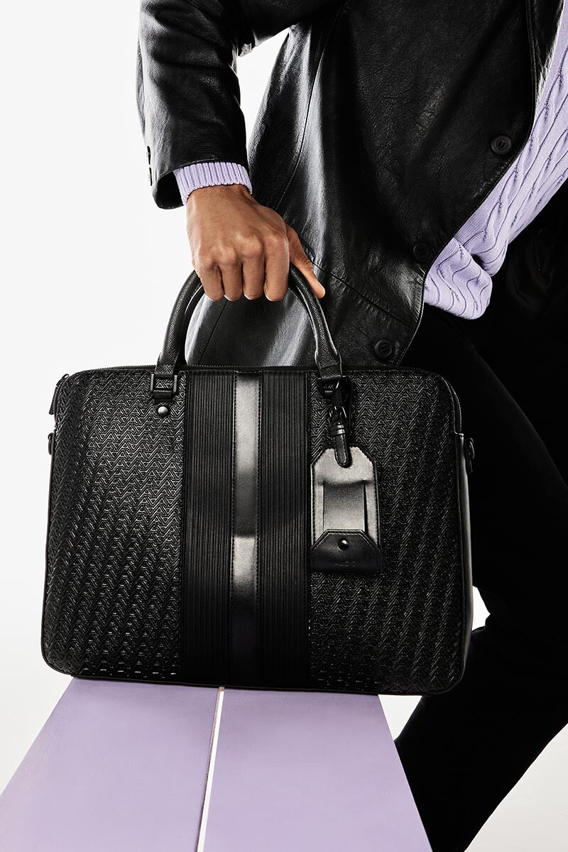 Man wearing a black handbag, with zipper clasp, short fashion handle and monogram print.