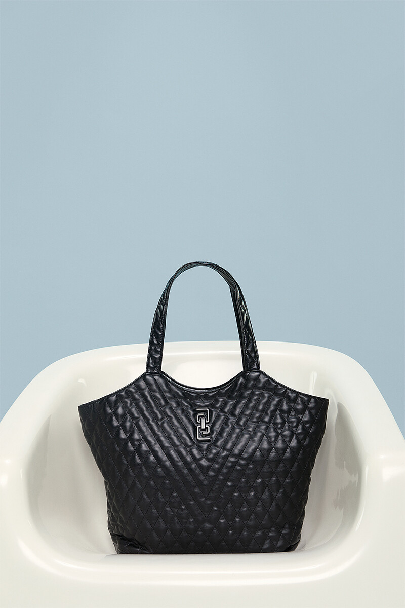 Black quilted tote bag with a monogram logo displayed in a minimalist setting.