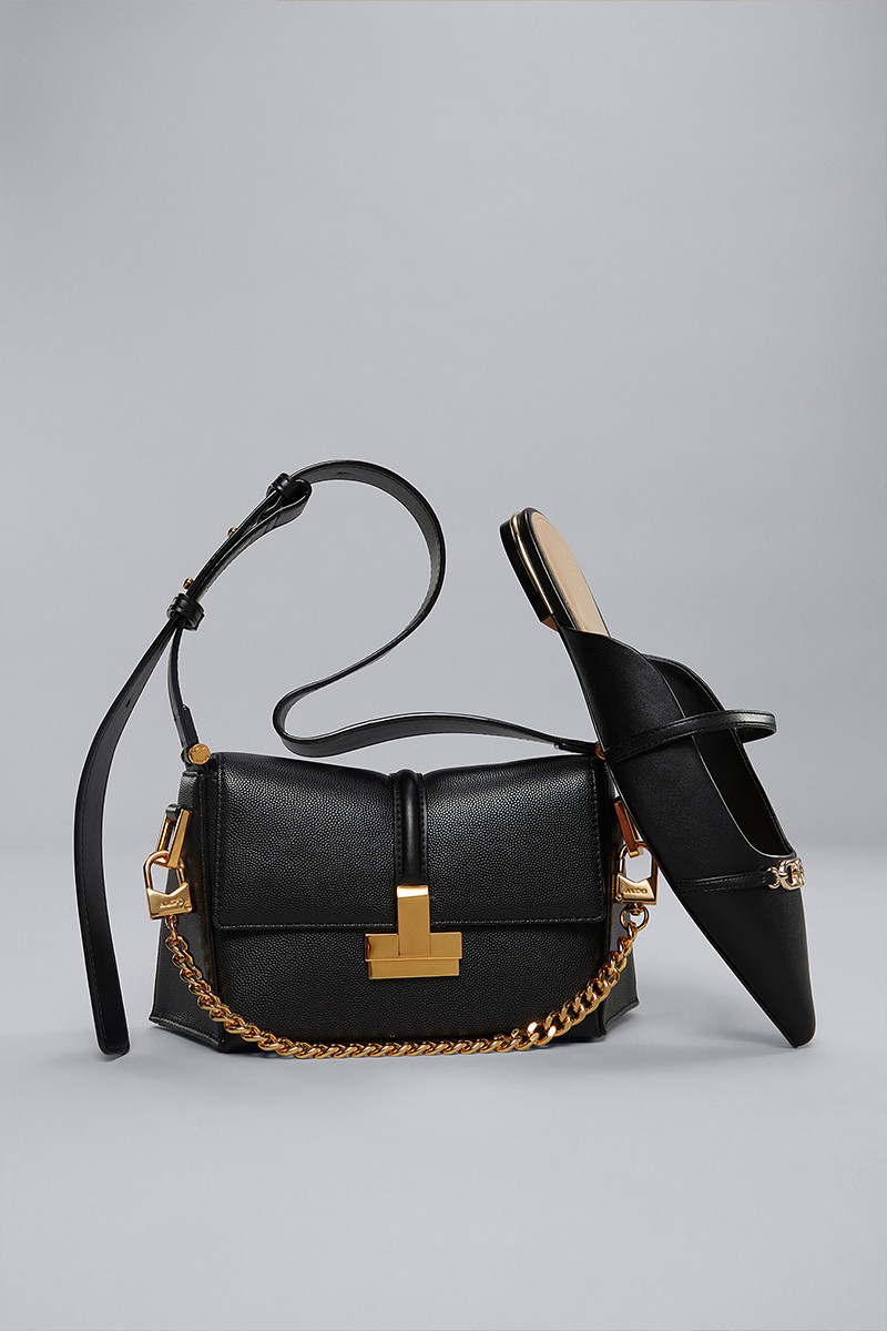 Black handbag with gold chain detailing paired with black pointed-toe flats featuring a matching gold accent.