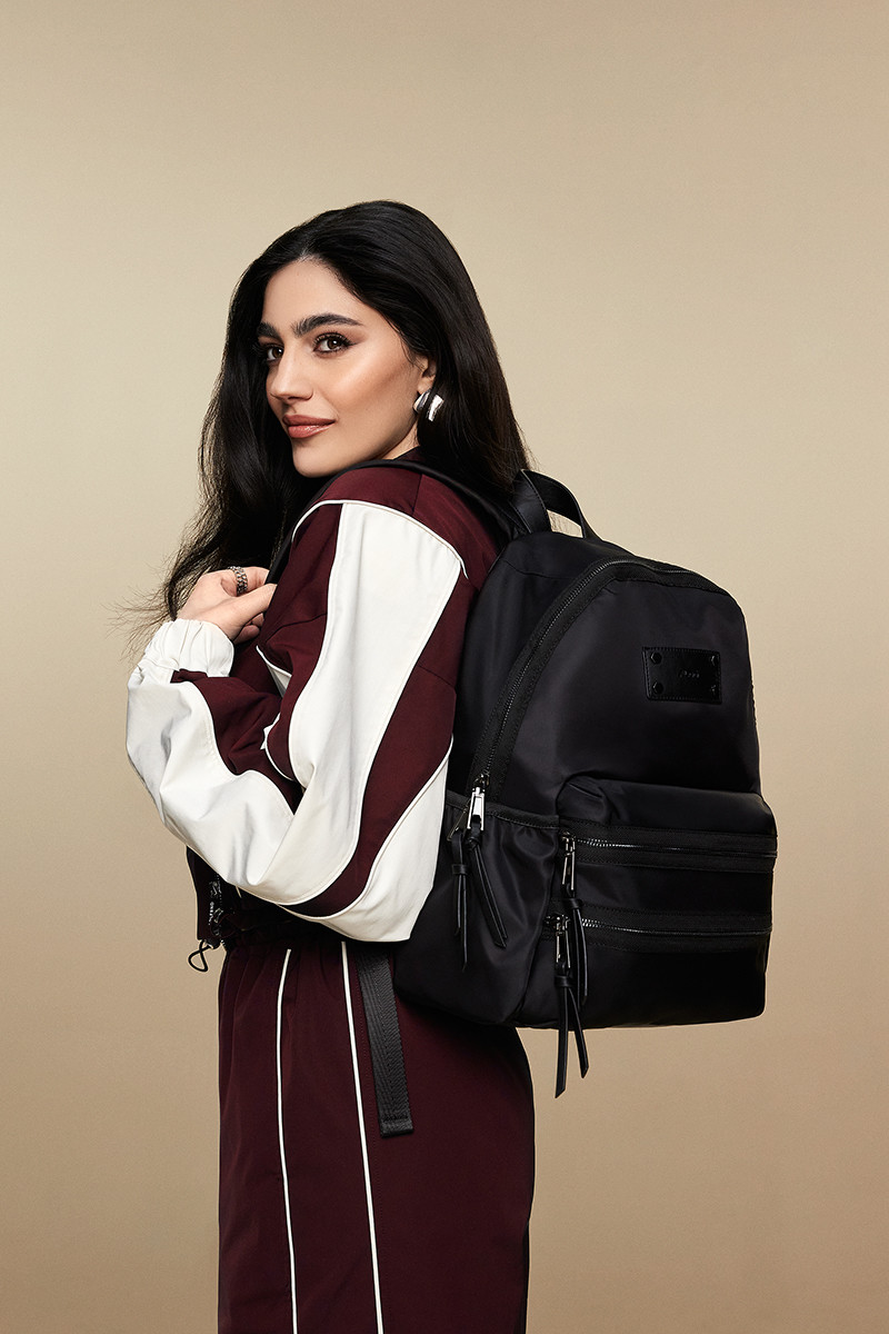 Woman in a burgundy and white tracksuit carrying a sleek black backpack.