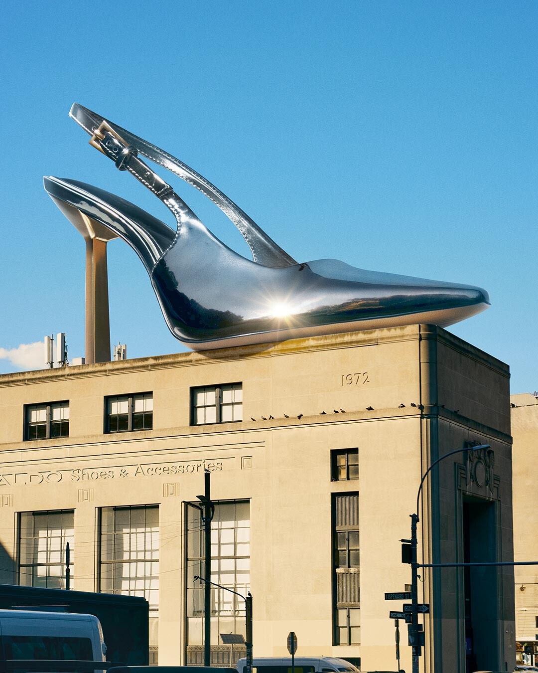 Shiny silver high-heeled slingback floating above a city building.