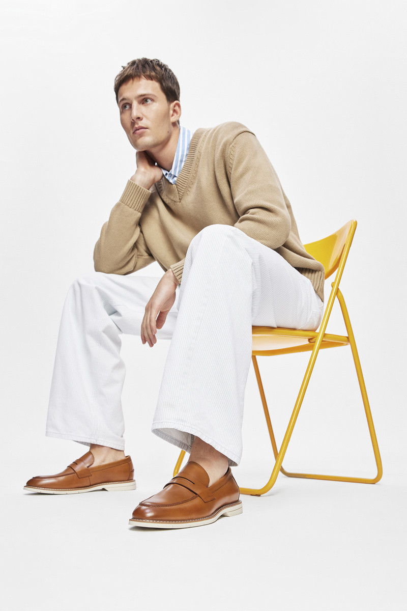 afro-descendant male model with crossed legs and an emphasis on the foot wearing a beige fabric sports shoe