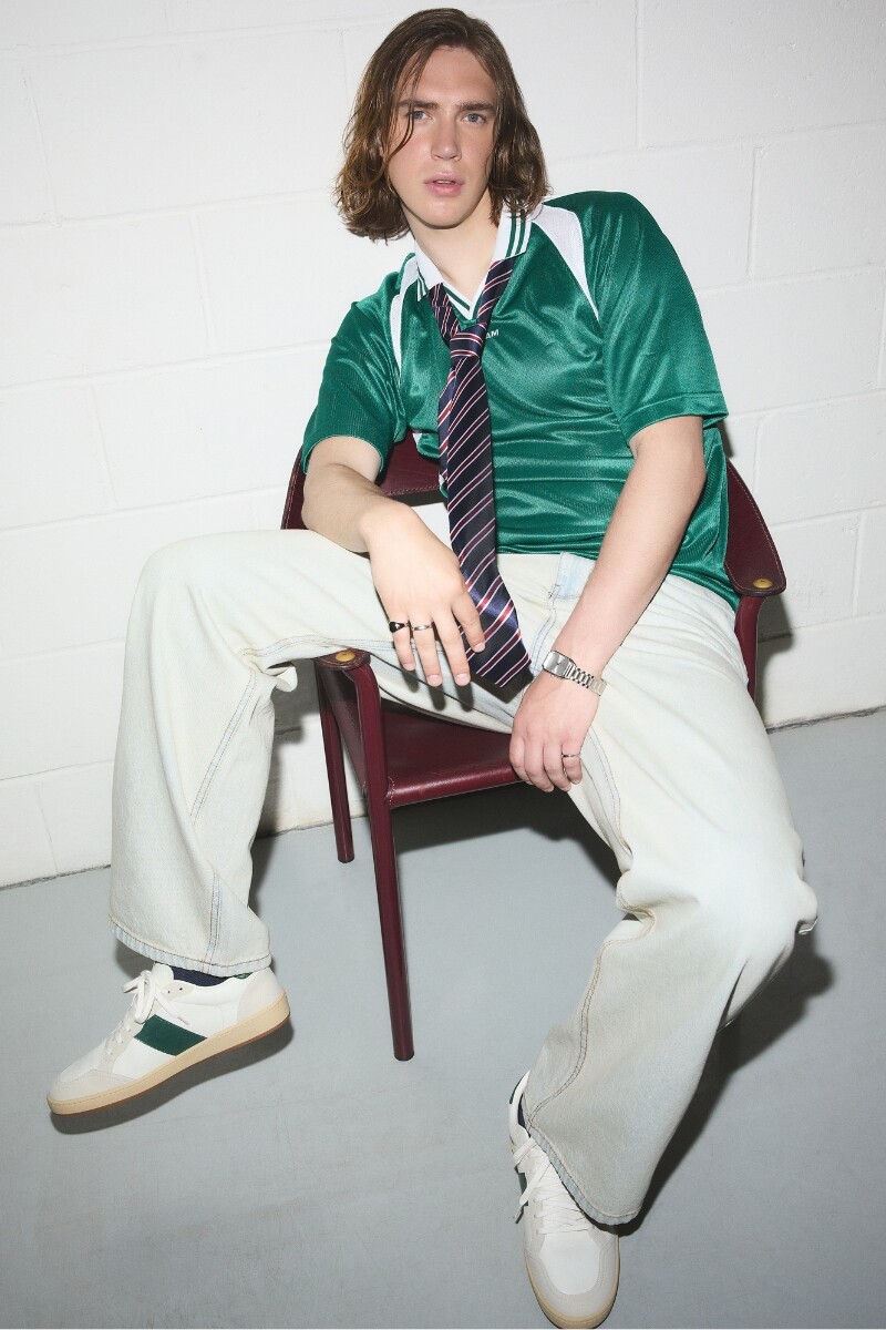 Man sitting wearing white and green sneakers with modern casual outfit.