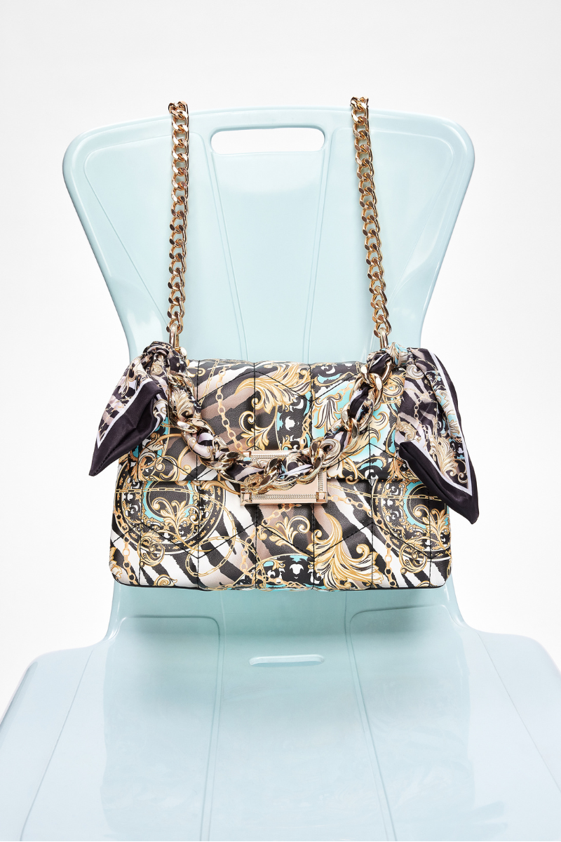 top handle bag with tropical and animal prints and a decorative chain and lace on a chair