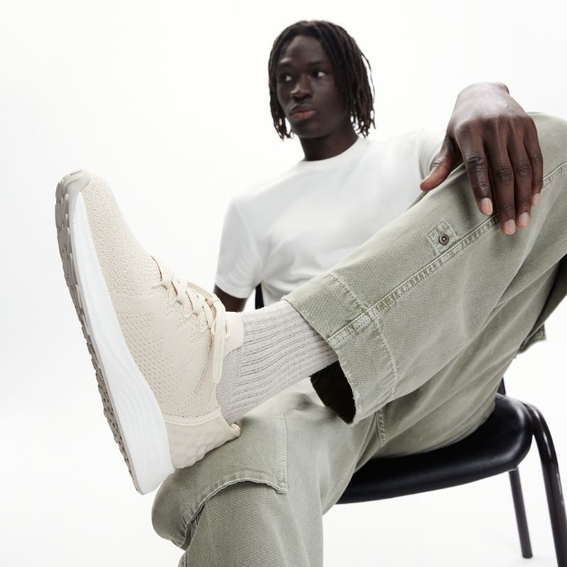 afro-descendant male model with crossed legs and an emphasis on the foot wearing a beige fabric sports shoe