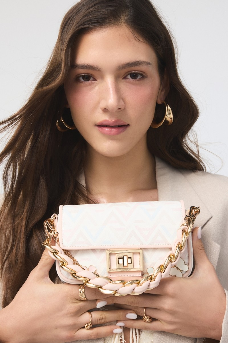 Model holding a light pink ALDO handbag with a gold chain and geometric pattern.
