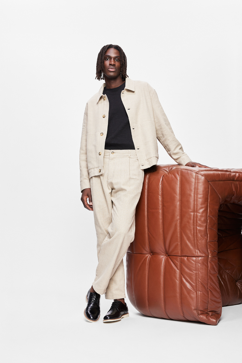 young afro-descendant model standing cross-legged on a brown leather sofa wearing black casual shoes