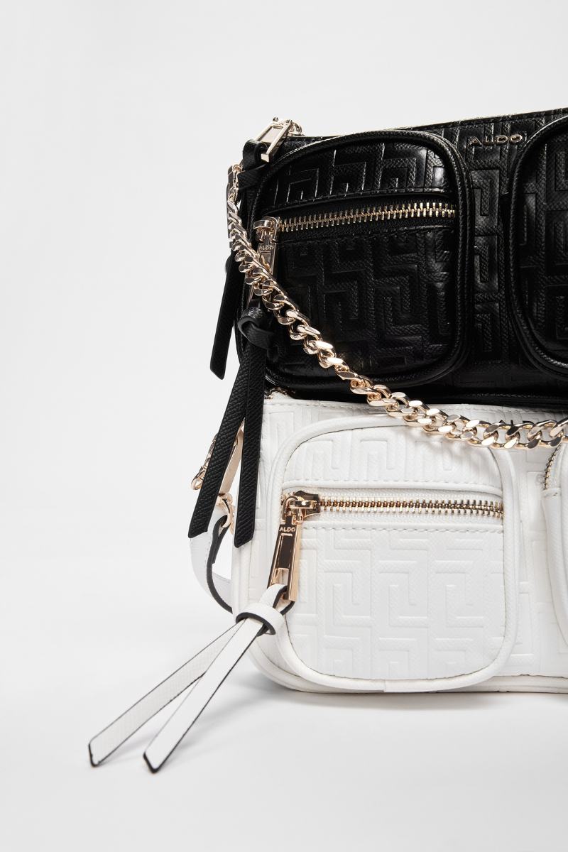 black bag on top of white bag, both shoulder bags with decorative texture and chains