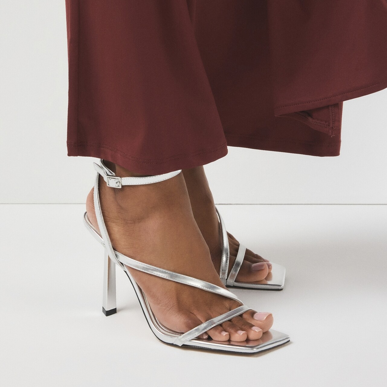Sapatos de salto alto prateados com tiras, usados com um vestido bordô.