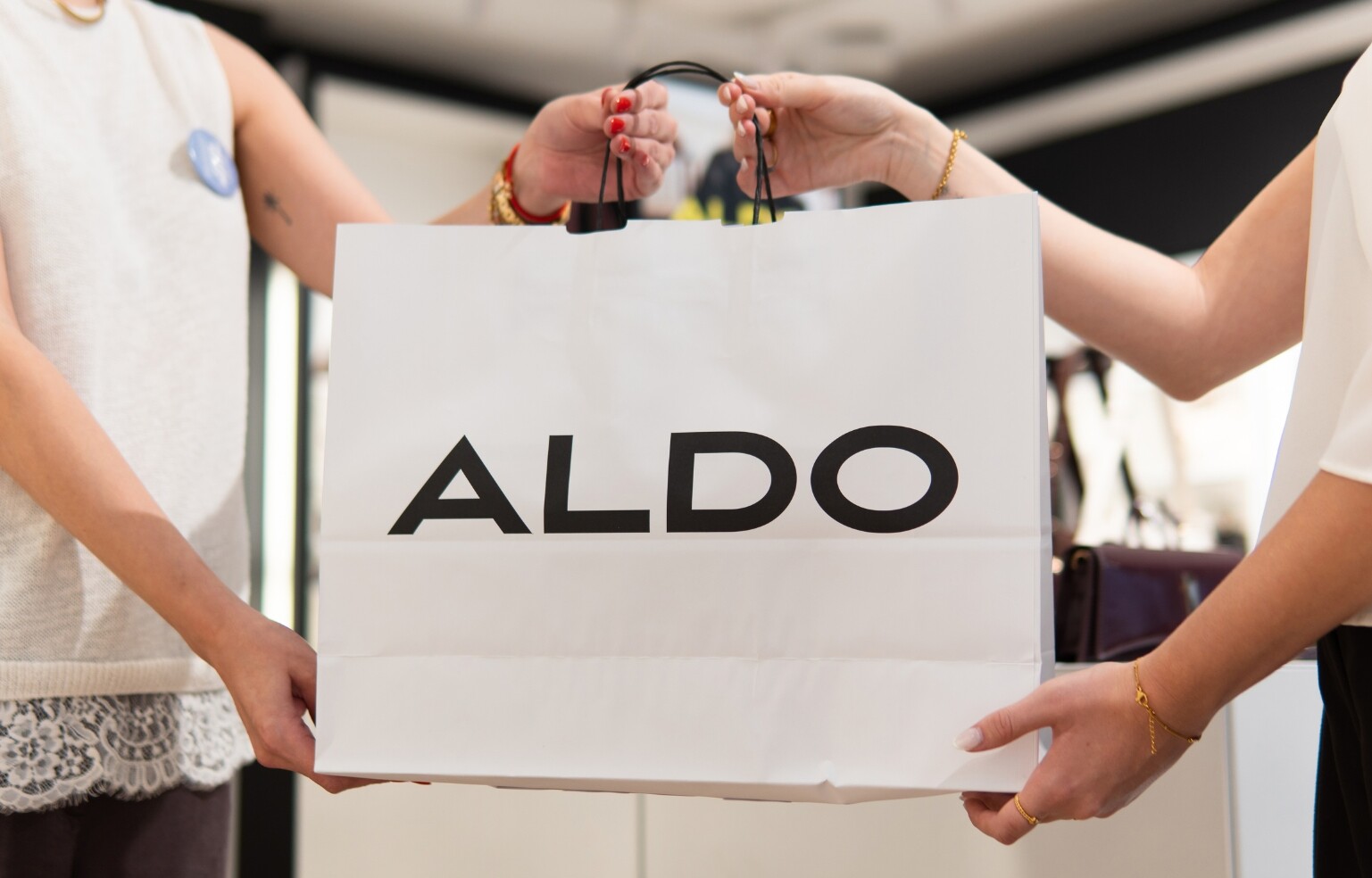 Duas pessoas a segurar um saco de compras branco com o logótipo da ALDO.