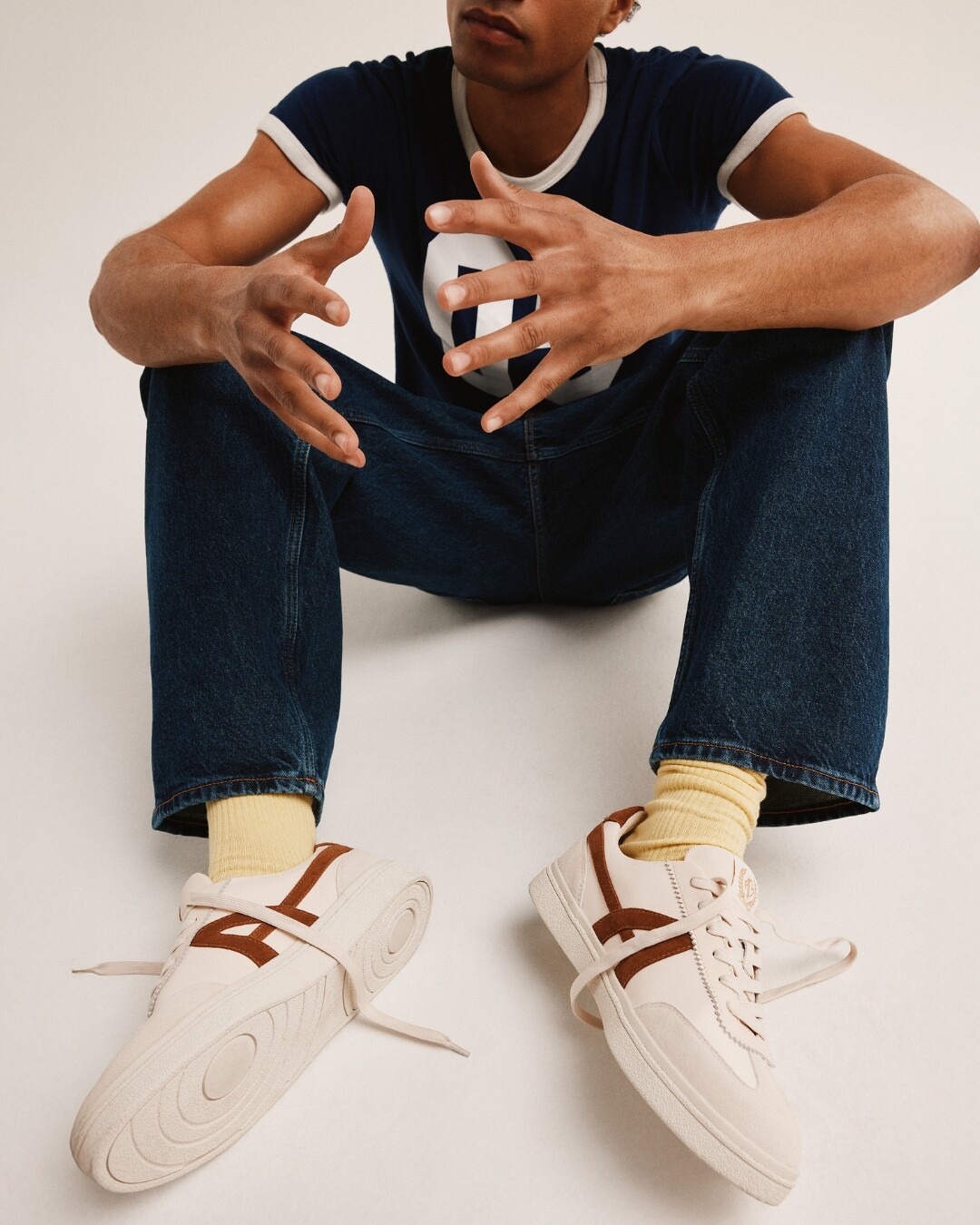 Hombre sentado con zapatillas blancas a rayas marrones.