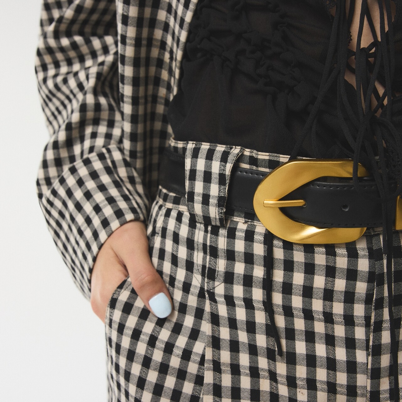 Detalle de cinturón negro con hebilla dorada sobre conjunto de cuadros.
