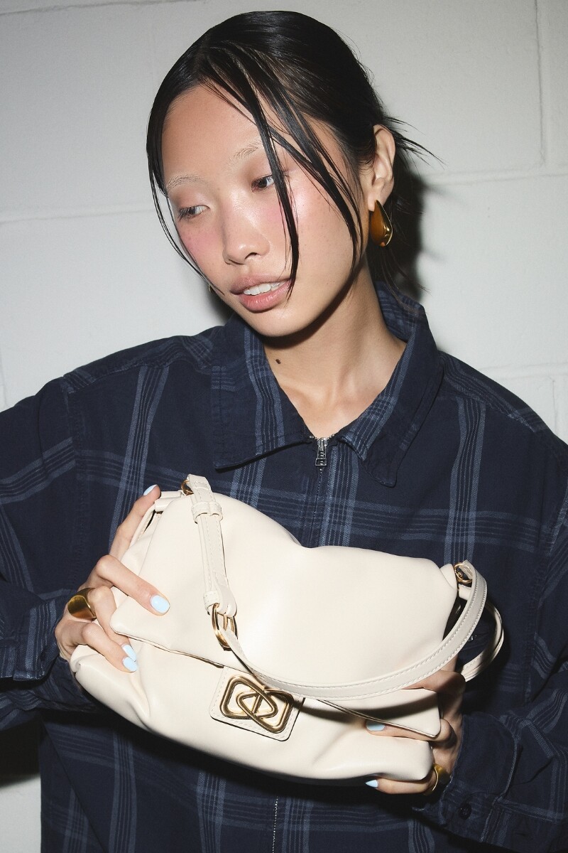 Mujer con bolso beige de hombro con detalle metálico dorado.