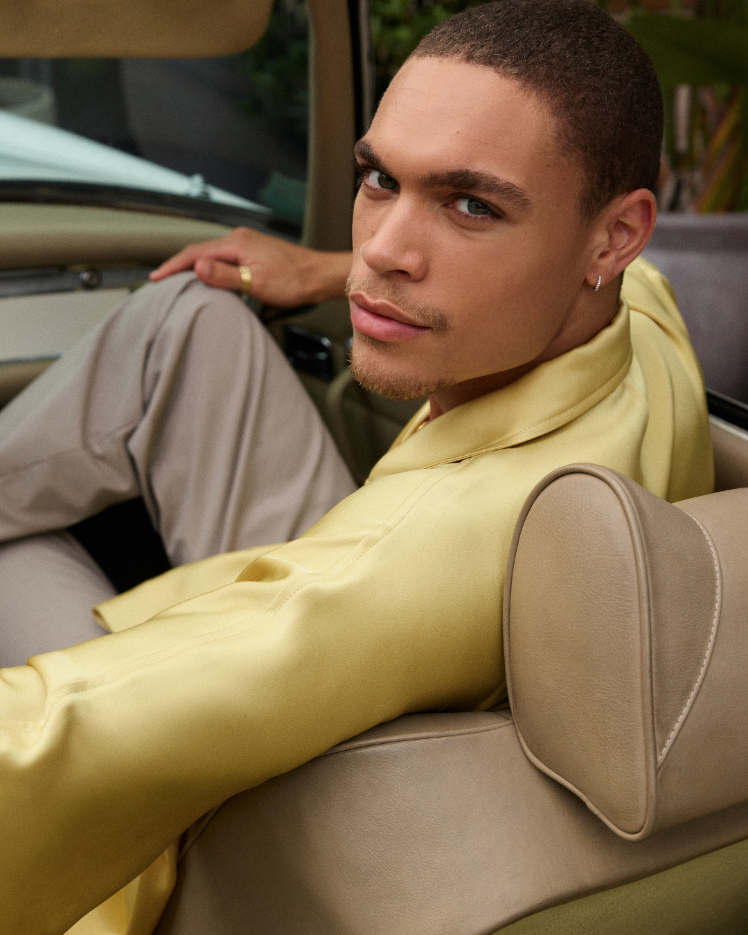 modelo masculino de camisa amarela e acessórios sentado confortável num carro conversível a olhar para trás