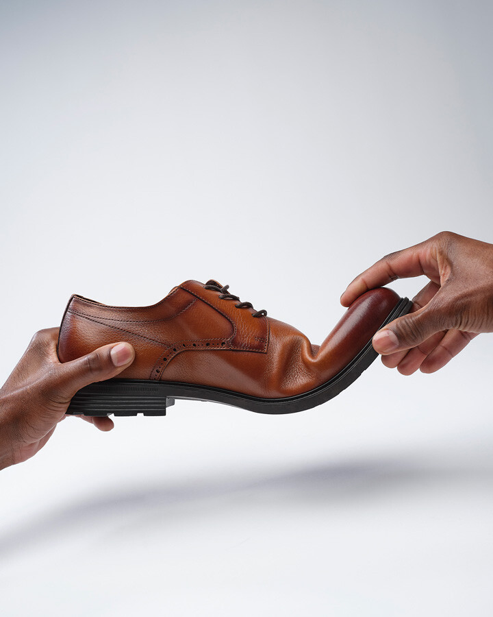 manos de hombre apretando zapatos de hombre marrón
