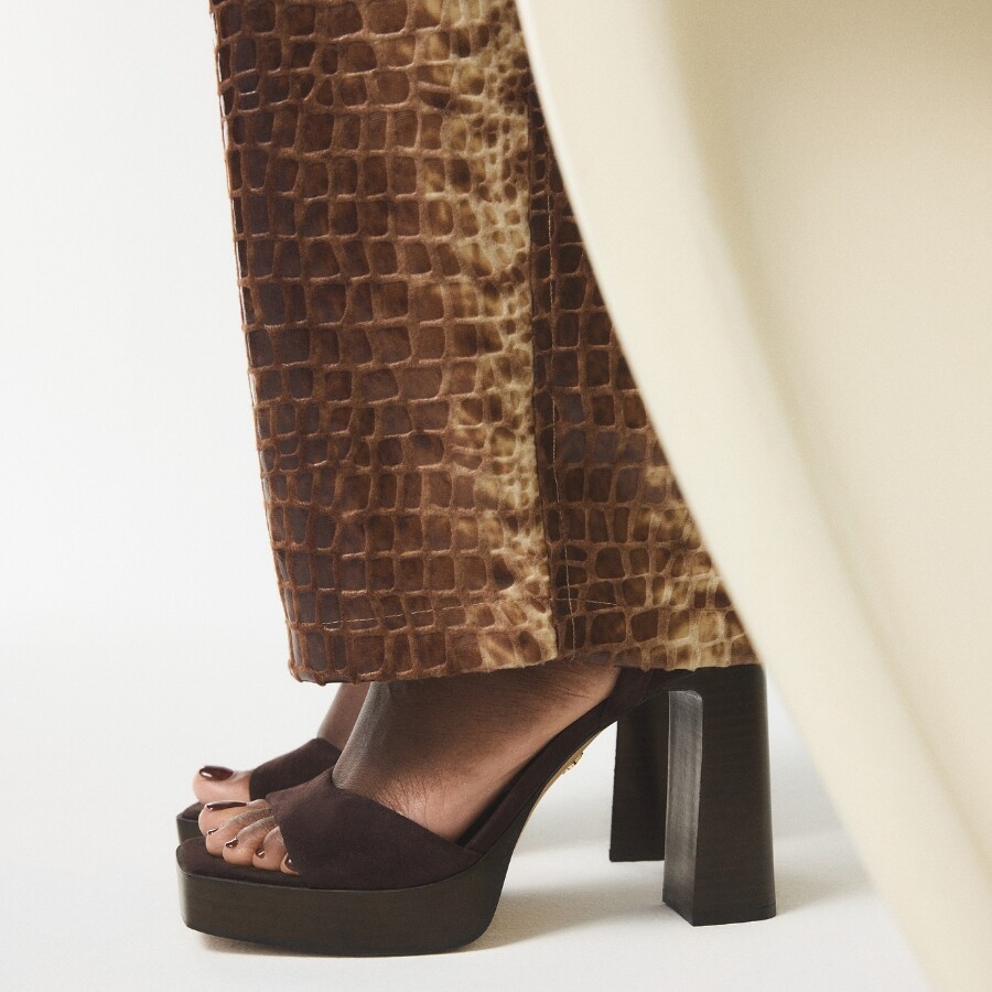 Sandalias de plataforma marrones con tiras anchas, combinadas con pantalones texturizados con estampado de cocodrilo marrón.