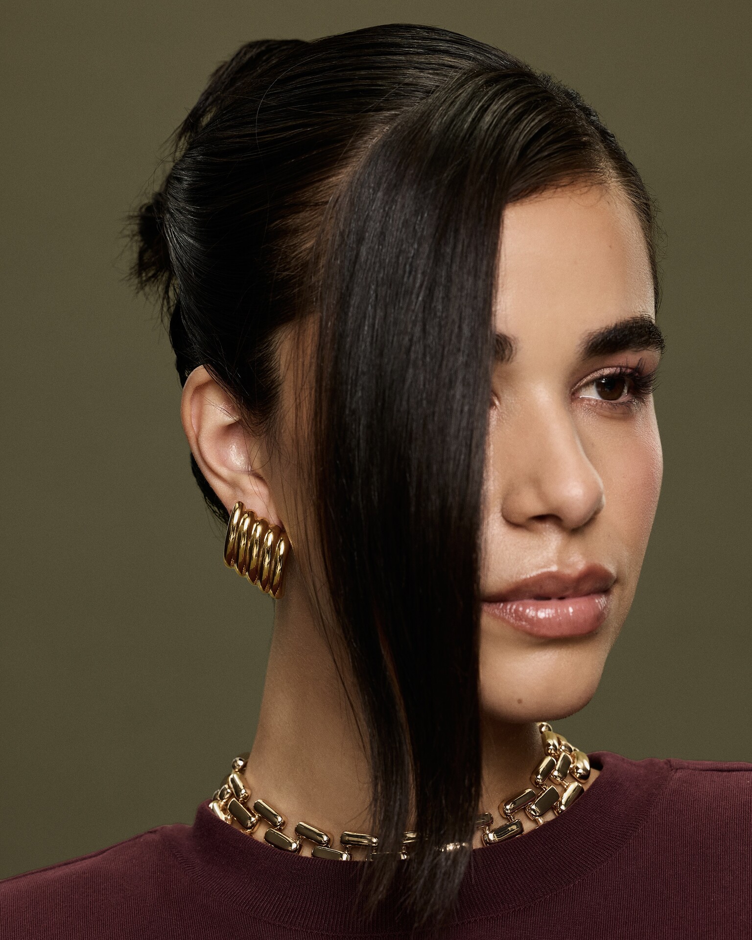 Mulher com franja, a olhar para o lado, a usar brincos dourados da ALDO e colar dourado da ALDO