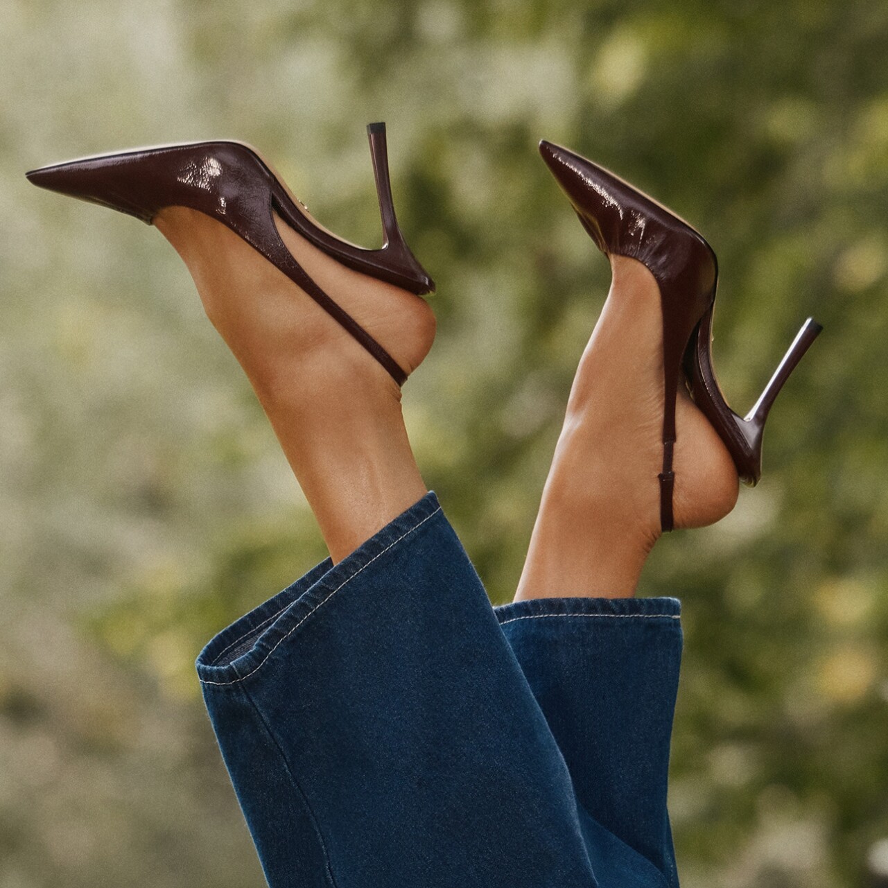 Zapatos de tacón marrones sobre fondo de árboles verdes.