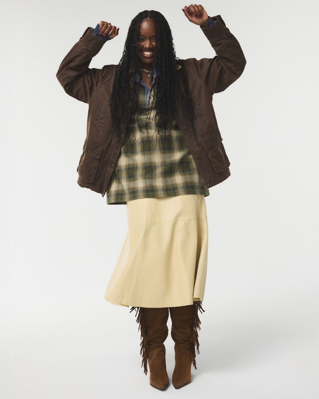 Mujer sonriente con chaqueta marrón y botas altas con flecos.