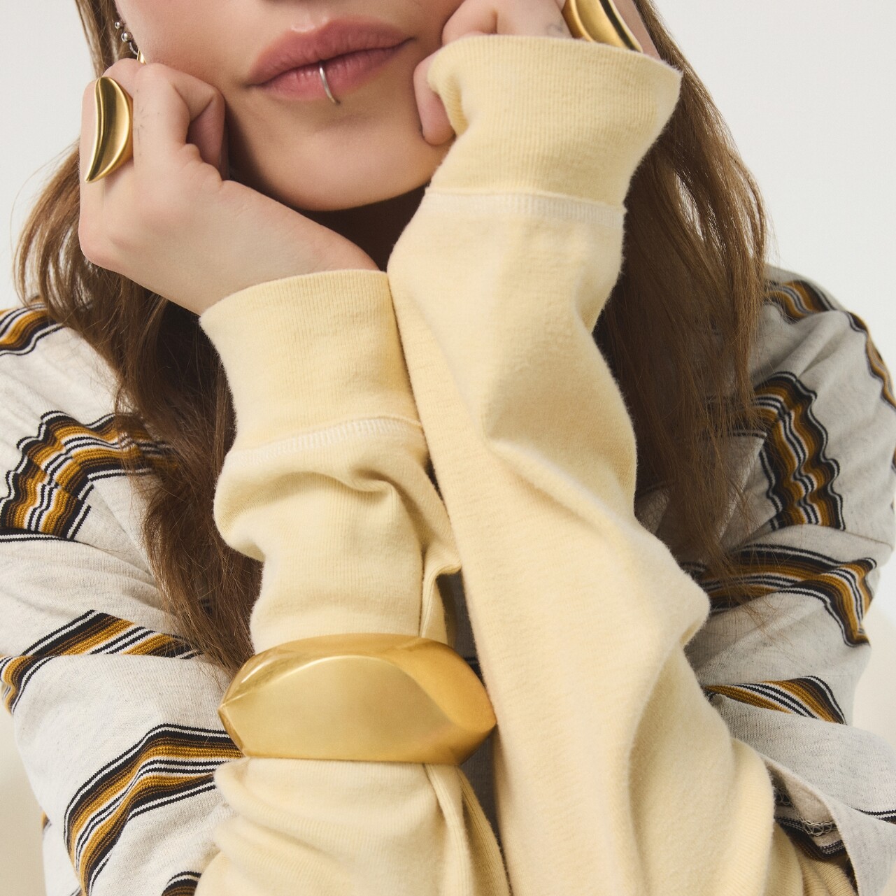 Mujer con joyas doradas de ALDO y suéter amarillo.