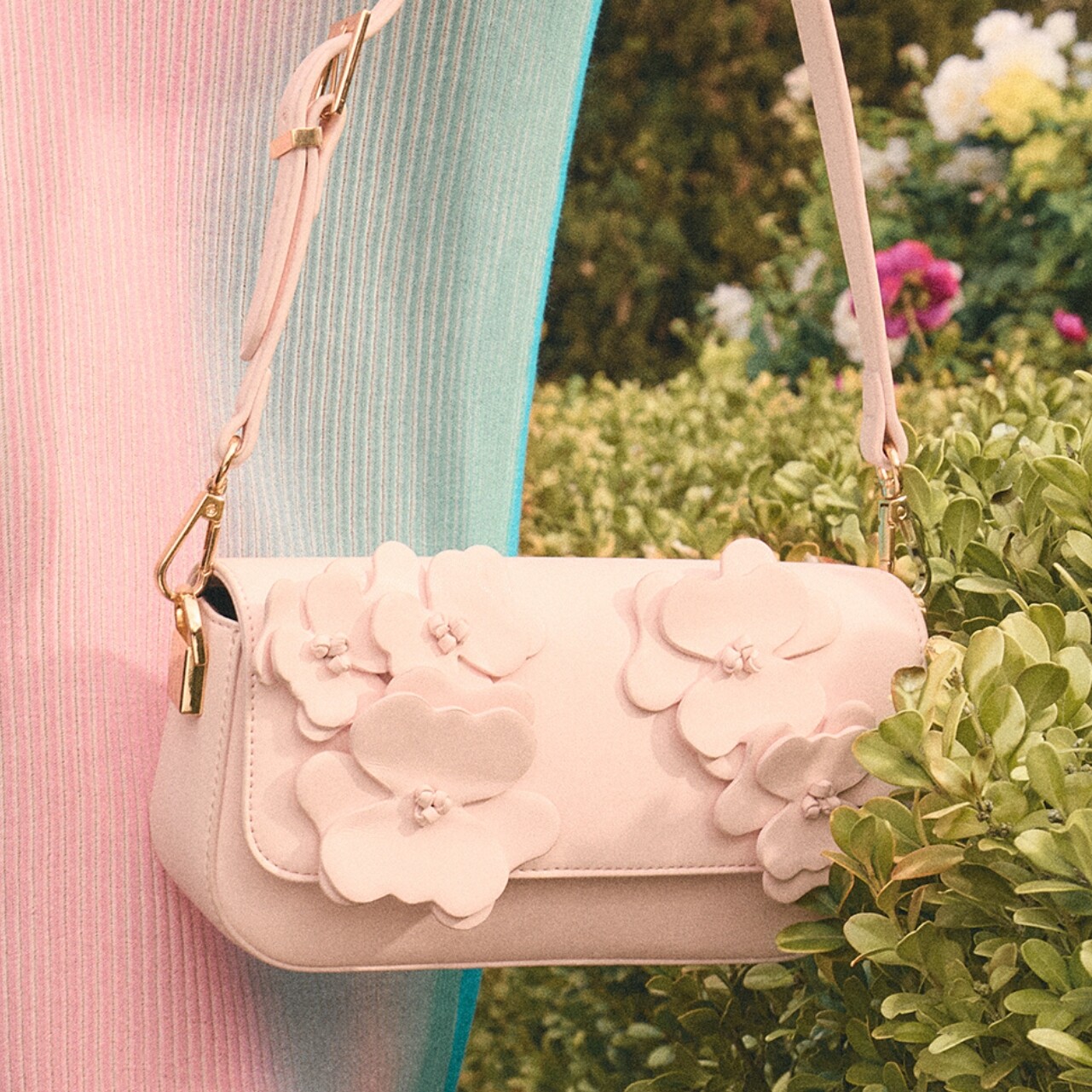 Mala cor-de-rosa com detalhes florais junto a um arbusto verde. 