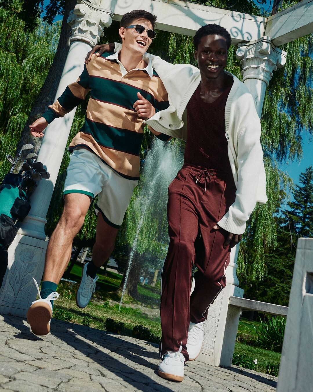 Dois homens a correr num parque verde, a partilhar um momento de exercício físico e divertido ao ar livre.