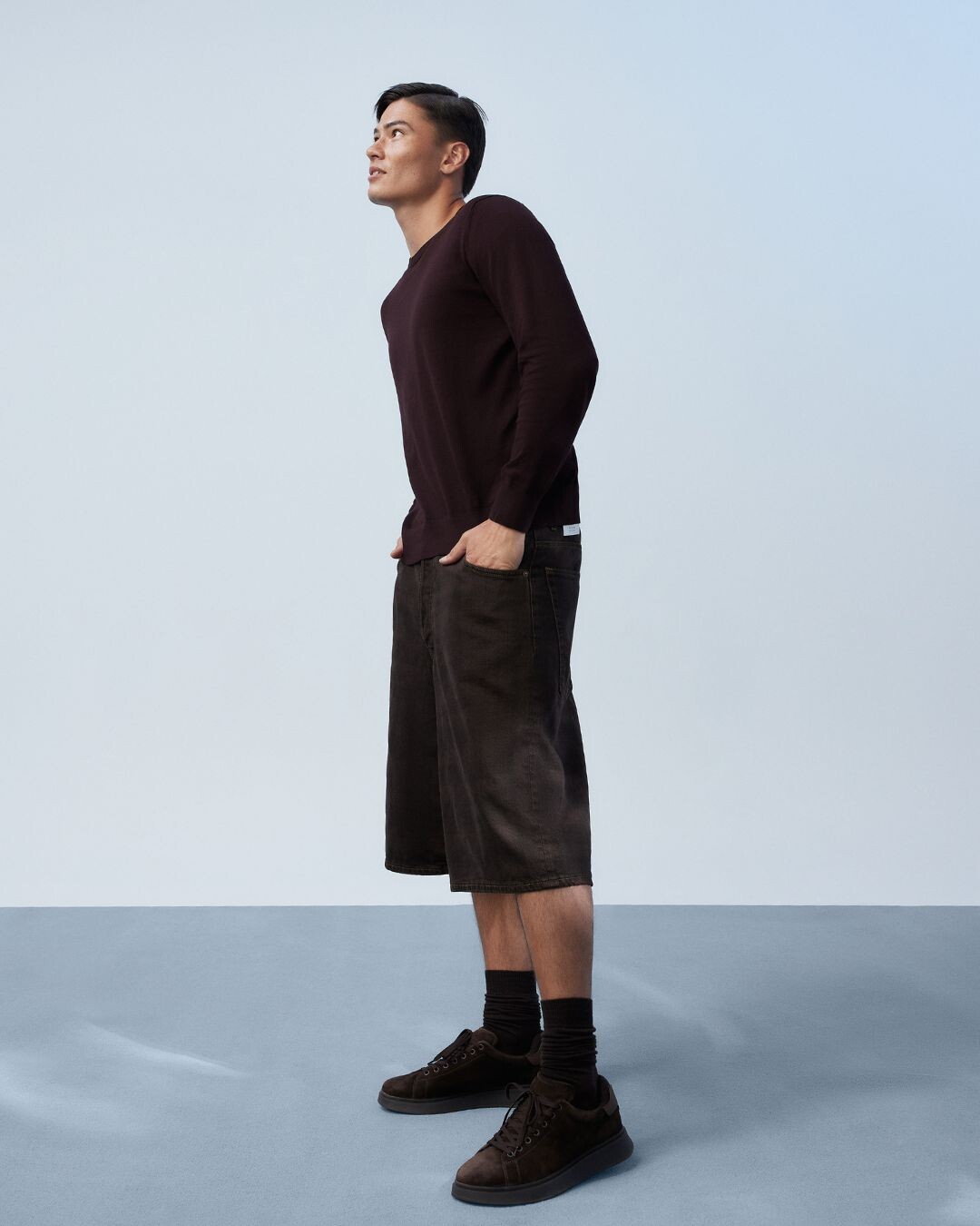 Homem vestido com camisola e calções castanhos, com sapatilhas castanhas ALDO.
