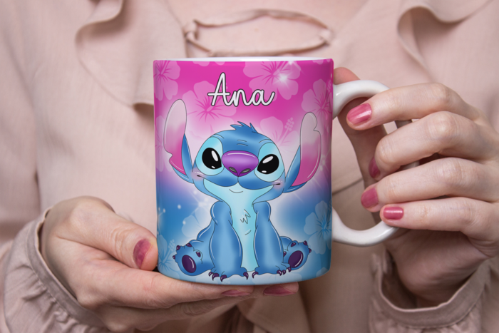 Zoom de uma pessoa a segurar numa caneca colorida com um personagem azul animado com olhos e orelhas grandes, de nome stitch A caneca tem fundo gradiente rosa a azul com detalhes florais e o nome 