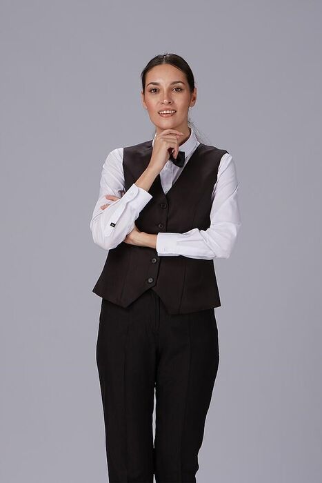 Mulher sorridente com colete preto, camisa branca e gravata borboleta, braços cruzados