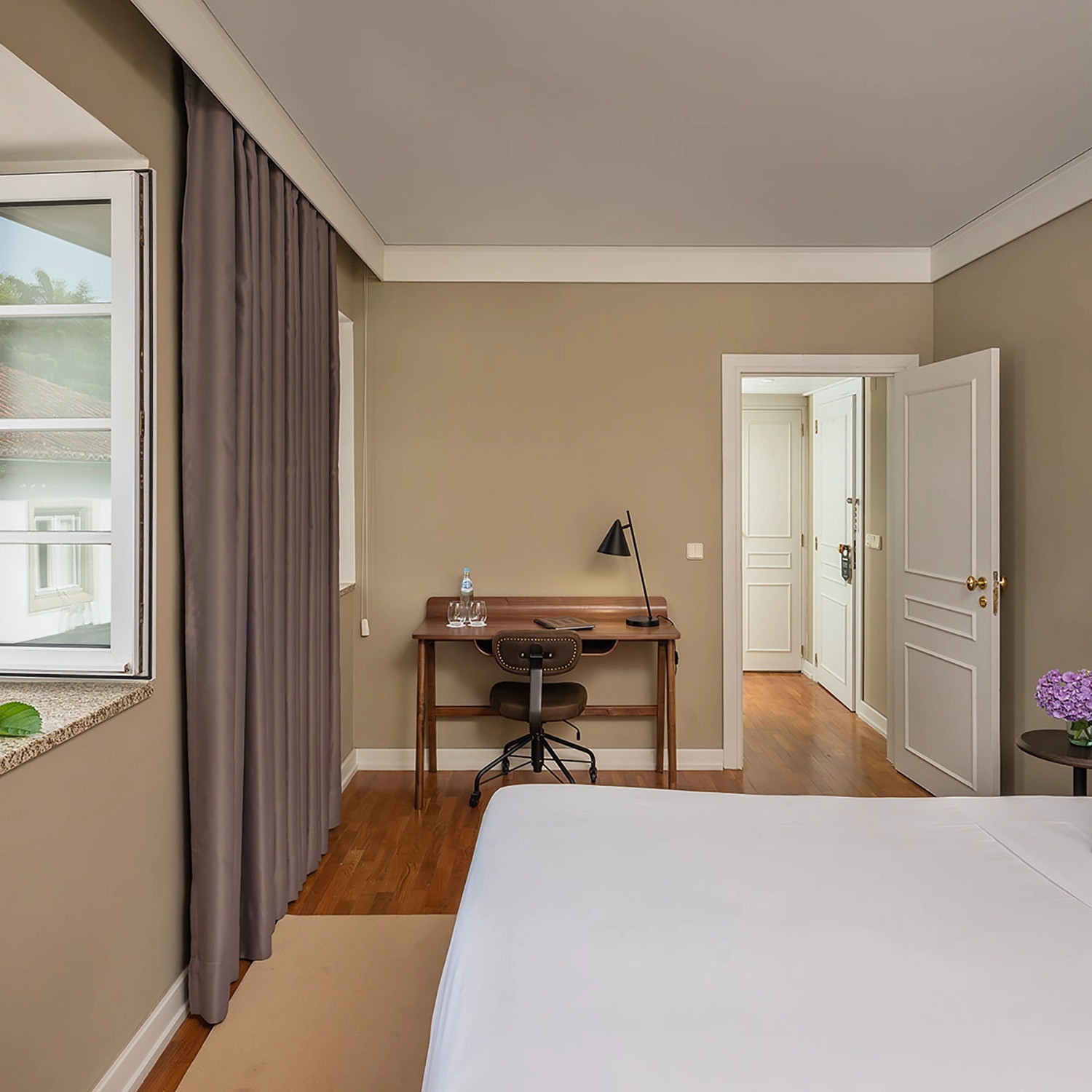 Quarto Classic luminoso com cama grande, secretária e decoração em tons neutros.