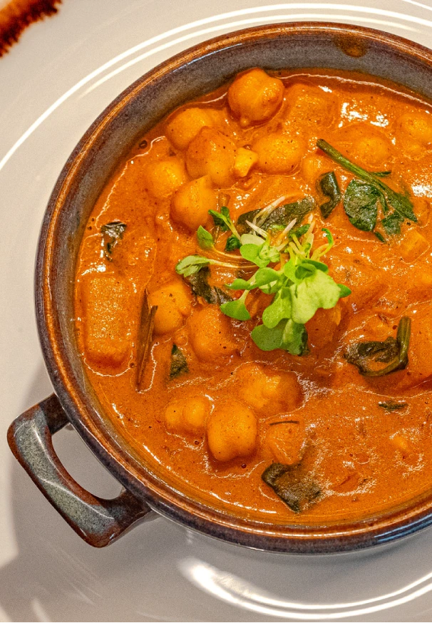 Vegan dish at Jardineiro – Vegan Kitchen in Porto, Portugal, featuring chickpeas and vegetables in a creamy tomato and spice sauce, garnished with fresh herbs from the chef’s menu. (desktop)