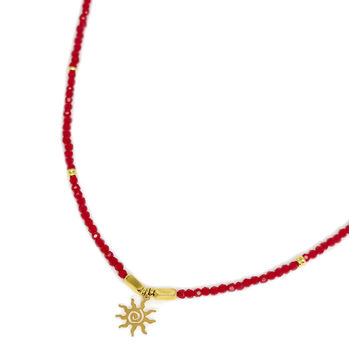 Colar Eugénio Campos pousado com contas vermelhas na malha e um pendente dourado em forma de sol.