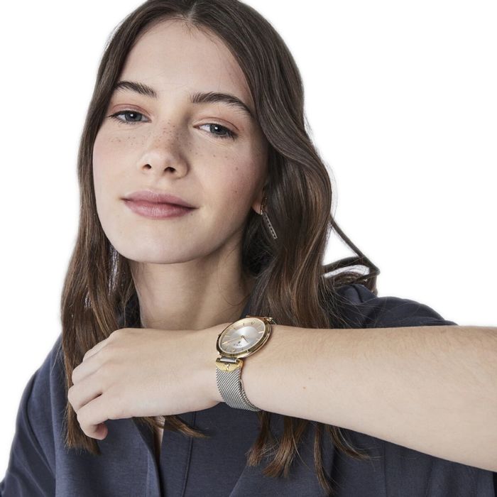 Modelo com um relógio Tous de bracelete prateada e bisel dourado com um mostrador analógico.