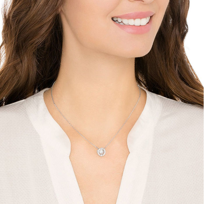 Modelo com um colar prateado Swarovski com um pendente com um cristal no centro e pedras à volta.