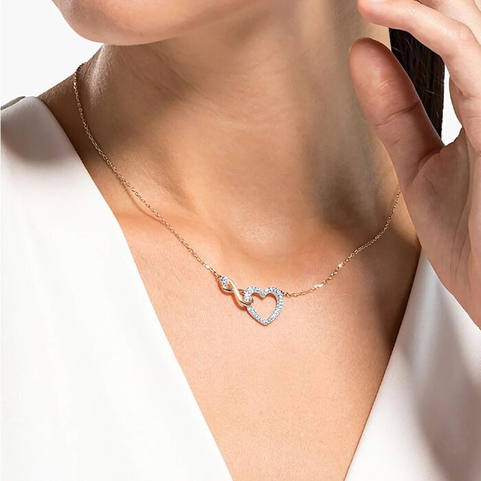 Modelo com um colar rose gold Swarovski com o símbolo inifinito e um coração prateado com pedras.