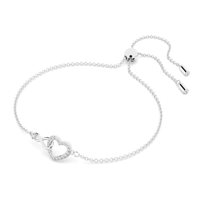 Pulseira prateada Swarovski, de lado, com o símbolo do infinito entrelaçado a um coração com pedras.