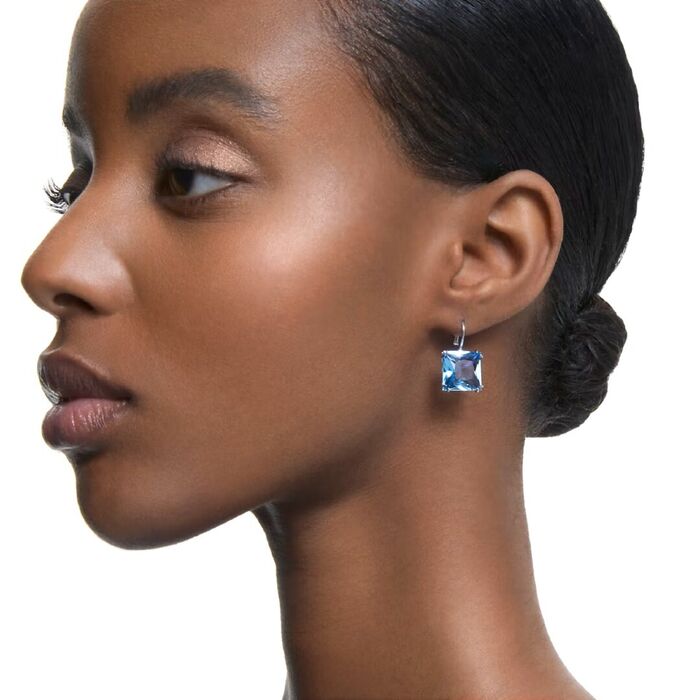 Modelo feminino com um brinco Swarovski prateado em formato argola com um cristal quadrangular azul.