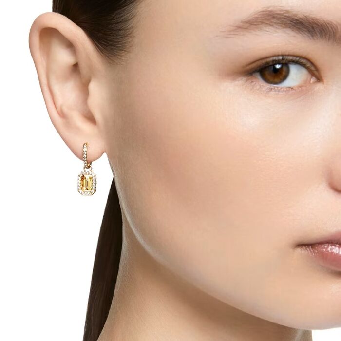 Modelo com uma argola dourada Swarovski com um pendente octogonal com cristais e uma pedra amarela.