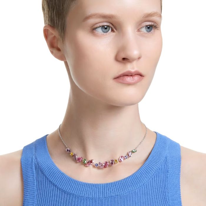 Modelo feminino com um colar prateado da Swarovski com cristais coloridos de diferentes formas.