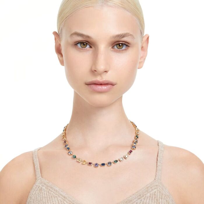 Modelo feminino com uma pulseira dourada Swarovski com cristais com diferentes formas e cores.