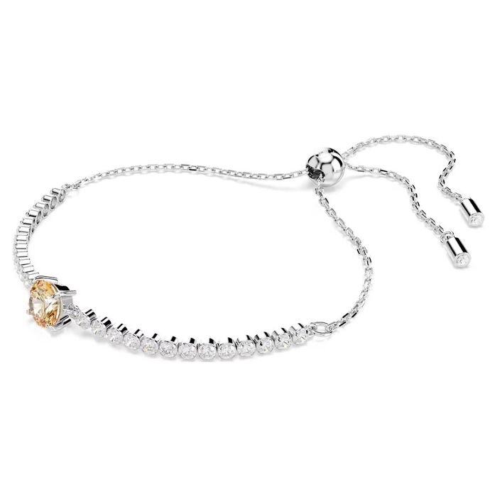 Pulseira prateada Swarovski, de lado, com cristais incolores e uma pedra amarela circular no centro.