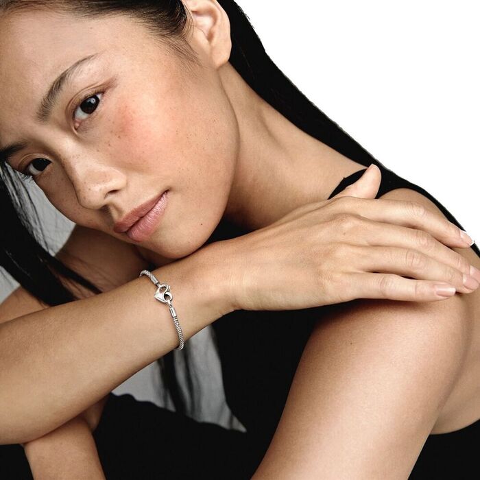Modelo com uma pulseira prateada Pandora com um fecho na forma de coração com o símbolo infinito.