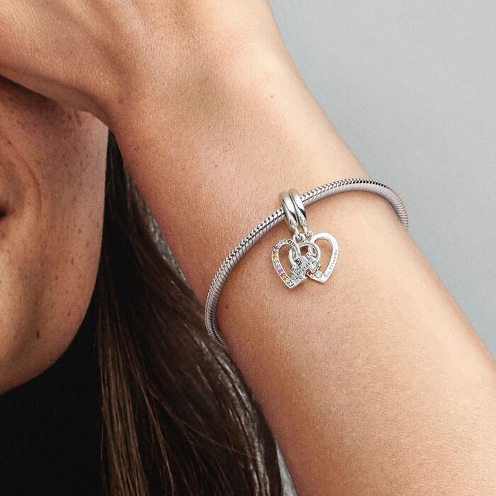 Modelo com a conta Pandora de dois pendentes de corações com pedras coloridos e uma peça de puzzle.