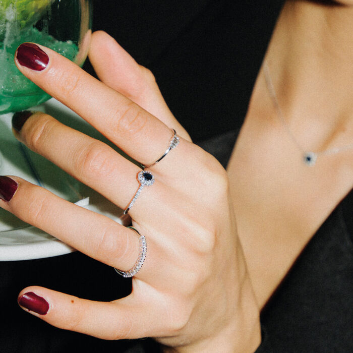 Mão feminina a usar anéis LECARRÉ em ouro branco, com diamantes, adornados com safira e esmeraldas.