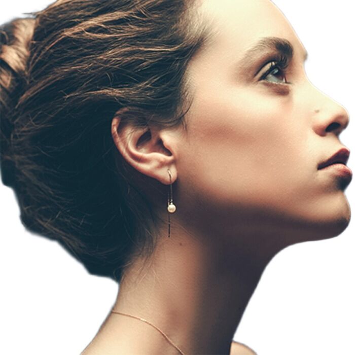 Modelo feminina com brinco LECARRÉ em ouro amarelo estilo pendente fino com pérola na ponta.