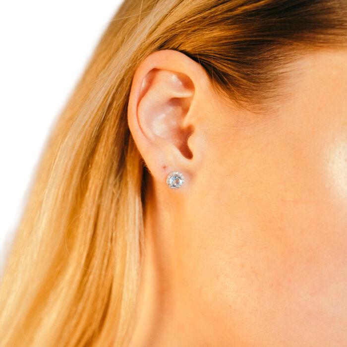 Modelo feminina a usar brinco Lecarré em ouro branco, com topázio azul e diamantes brancos ao redor.