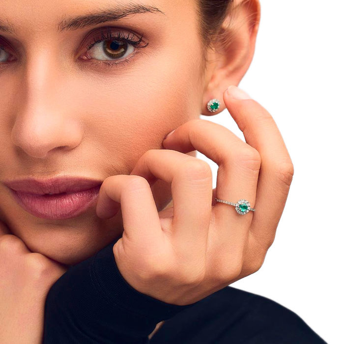 Modelo feminina de brinco e anel LECARRÉ em ouro branco com diamantes cravados à volta de esmeralda.