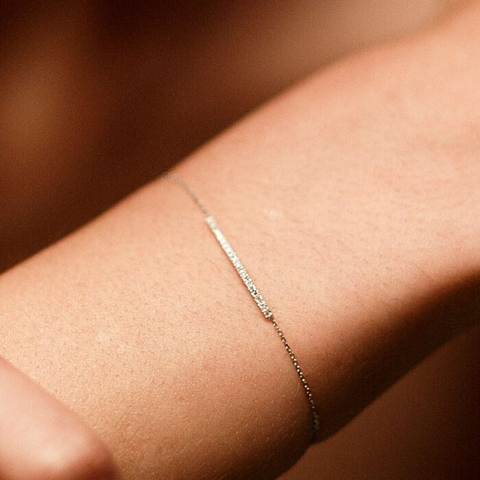Pulso feminino com pulseira Lecarré em ouro de 18k, com barra ao centro, cravada de diamantes.