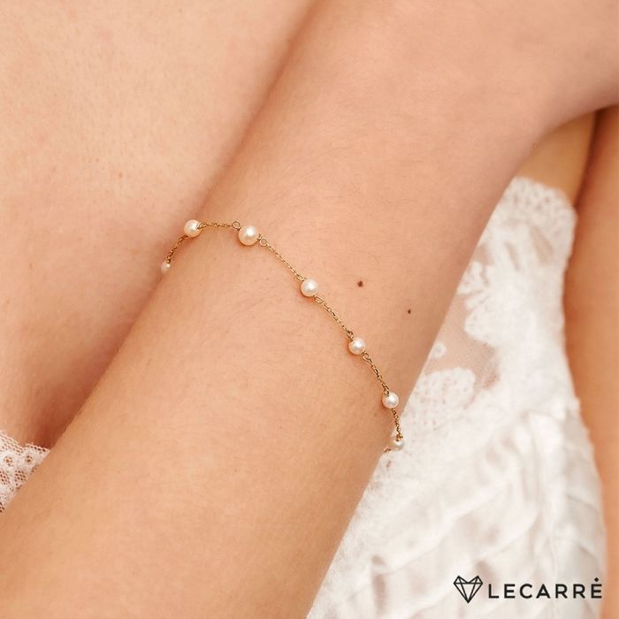 Pulso feminino com pulseira Lecarré em ouro de 18k, dourada, com pérolas redondas intercaladas.
