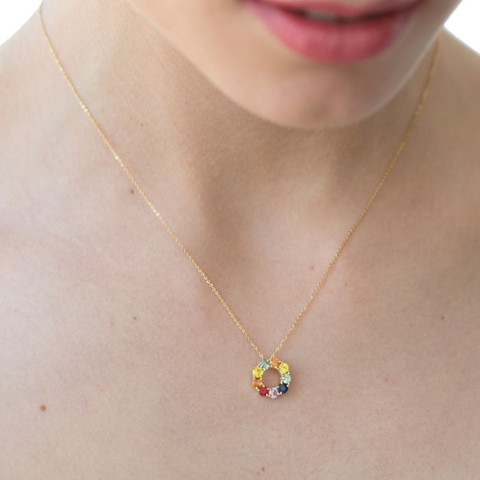 Modelo feminina com colar em ouro amarelo, com safiras coloridas que formam um círculo pendente.